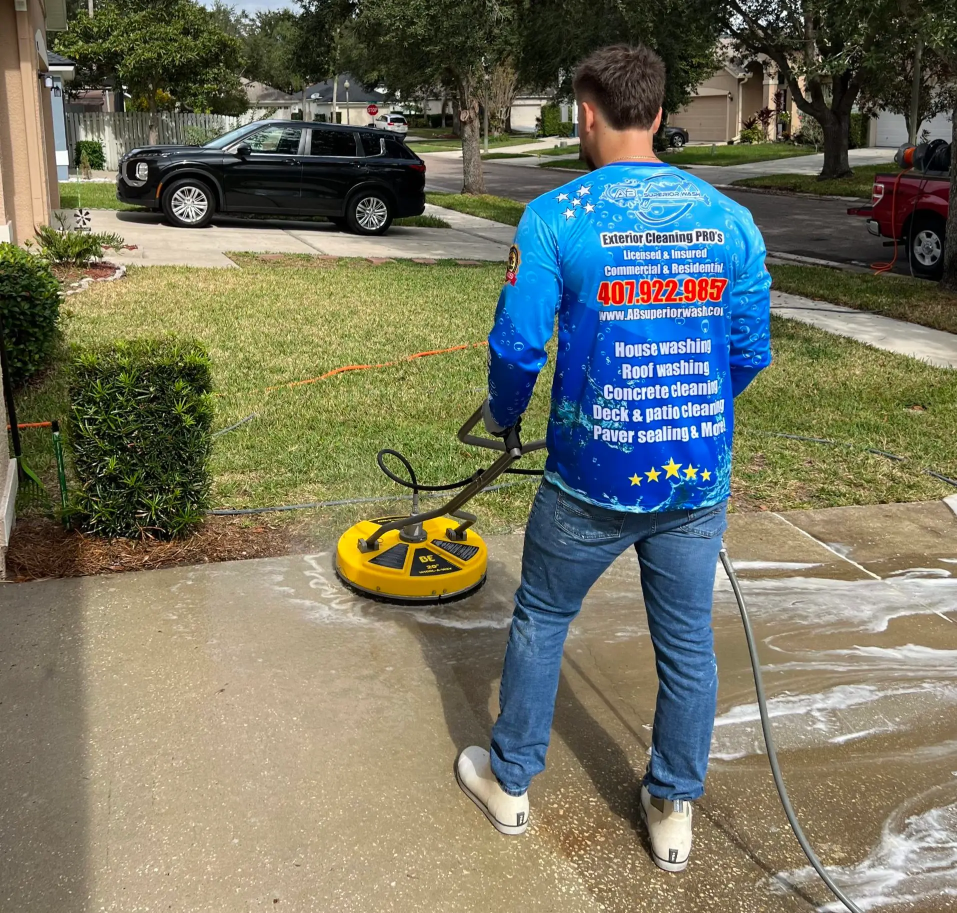 AB Superior Wash technician in a branded jersey running a surface cleaner on a concrete driveway in Orlando