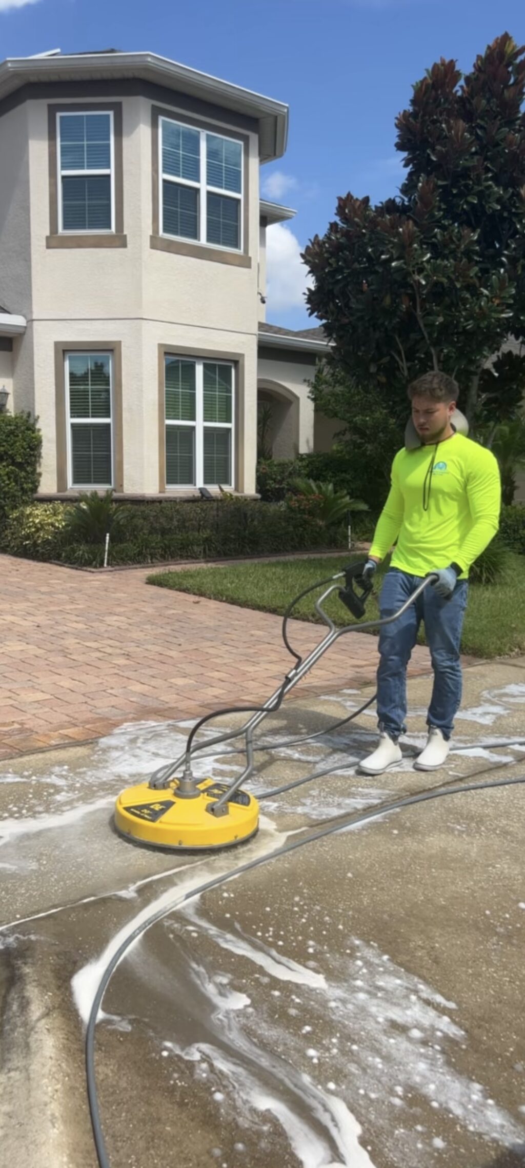 AB Superior Wash technician in a hi-vis branded shirt running a surface cleaner on a foamed driveway in Orlando