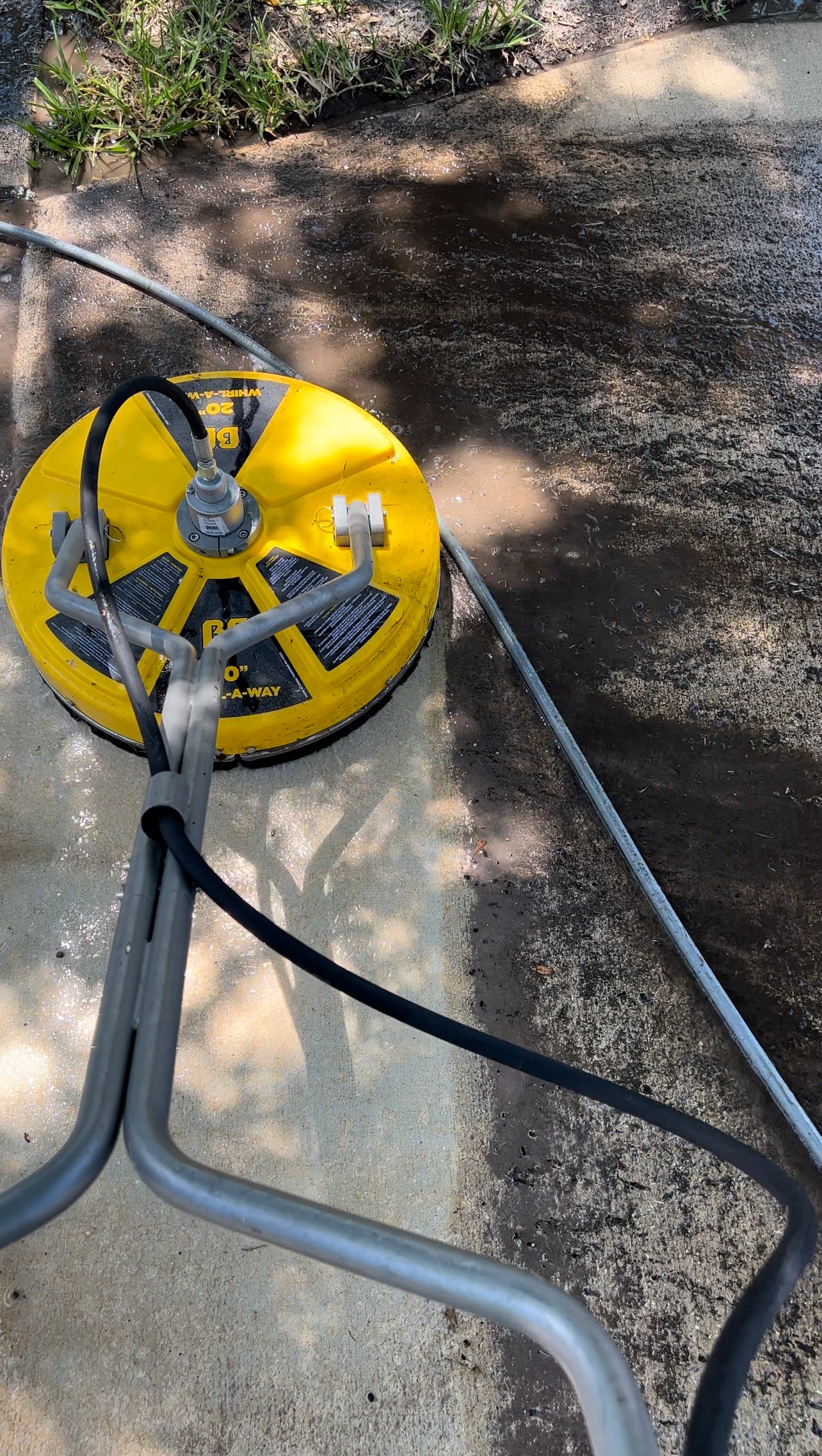 A surface cleaner mid-pass on concrete in Orlando, clean bright stripe next to heavy dark algae and grime